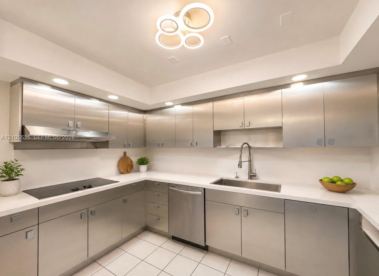 Contemporary kitchen featuring stainless steel cabinetry, white countertops, integrated cooktop, stainless steel range hood, and a modern ceiling ligh