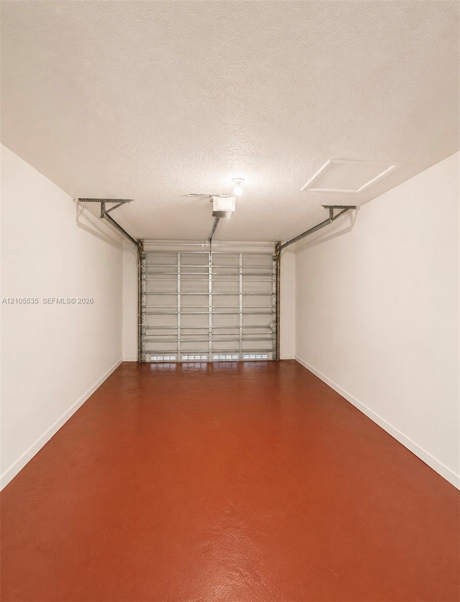 Garage with a sealed concrete floor, automatic garage door opener, and a ceiling-mounted light fixture