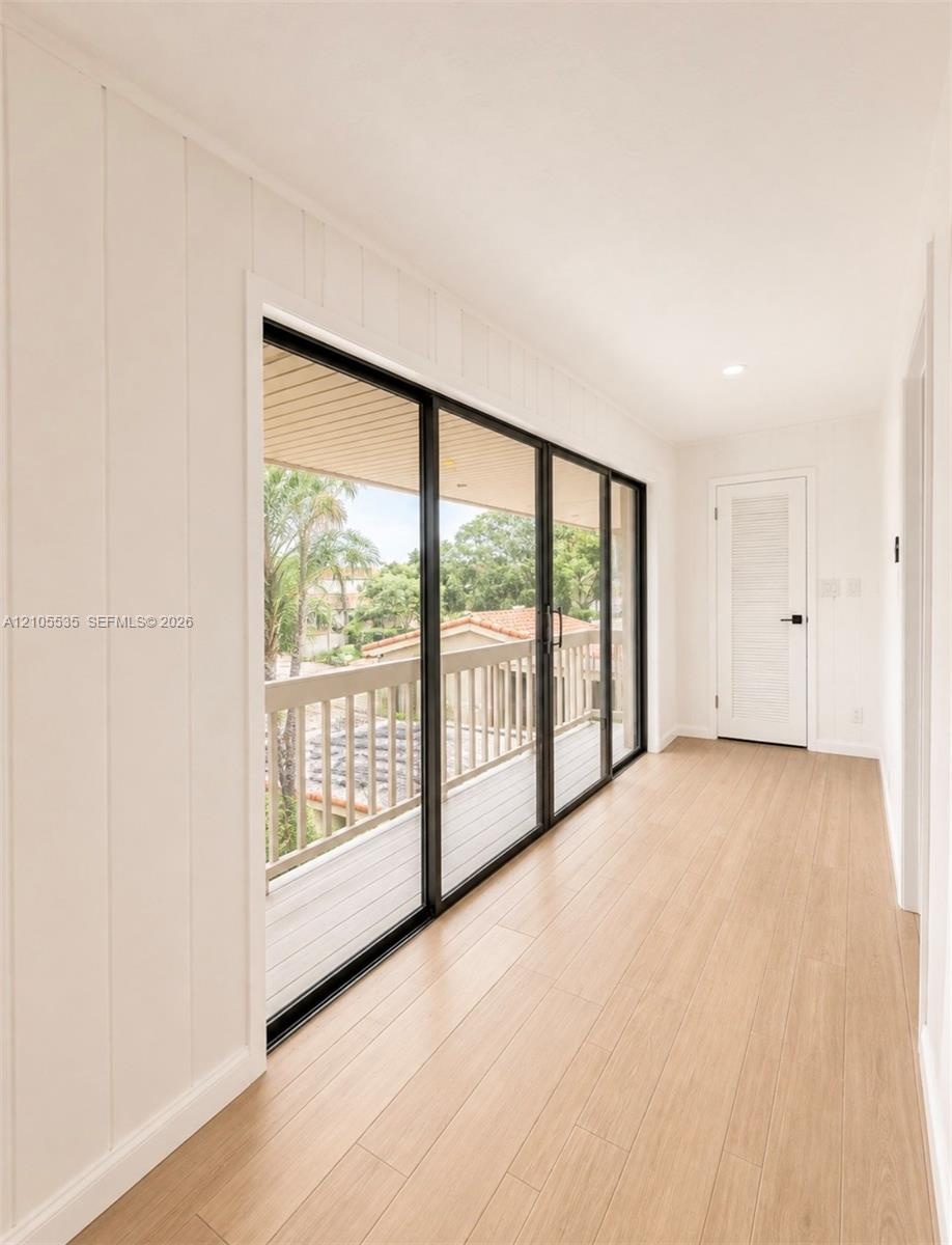 Recessed lighting, wood-finish flooring, white paneled walls, white paneled door with black hardware, and multi-panel sliding glass doors accessing an