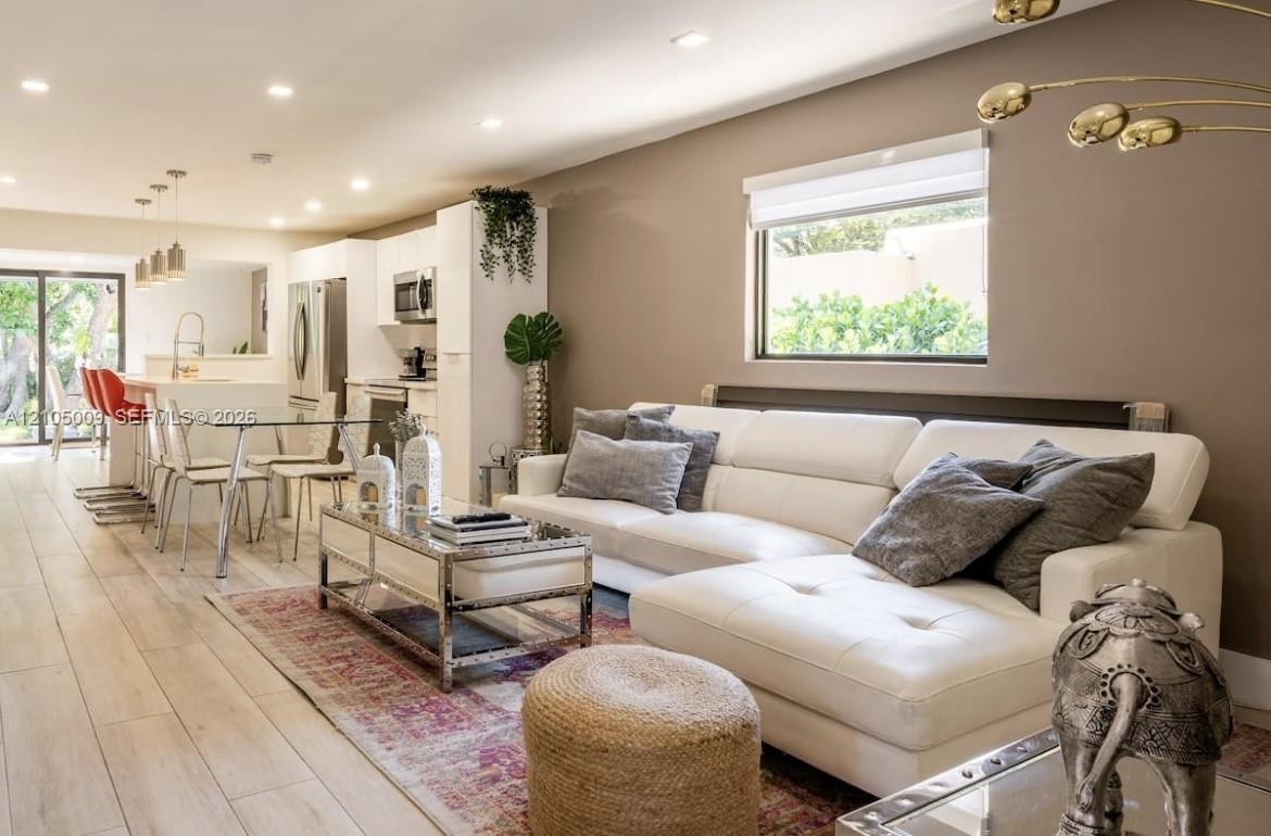 Open-concept living area with light wood-finish flooring, recessed lighting, and a kitchen featuring stainless steel appliances