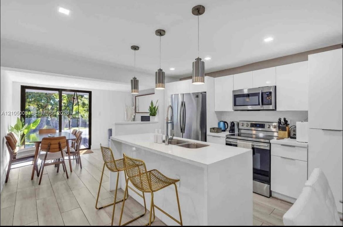 Contemporary kitchen featuring white cabinetry, stainless steel appliances, and a central island with an integrated sink