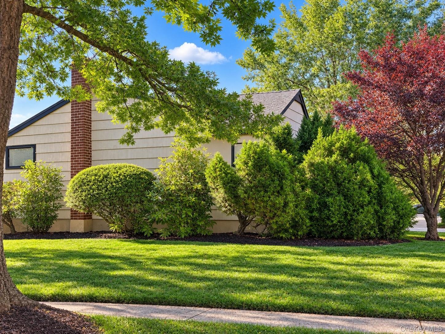 Manicured lawn, mature trees, and established shrubbery complement the exterior siding and brick chimney