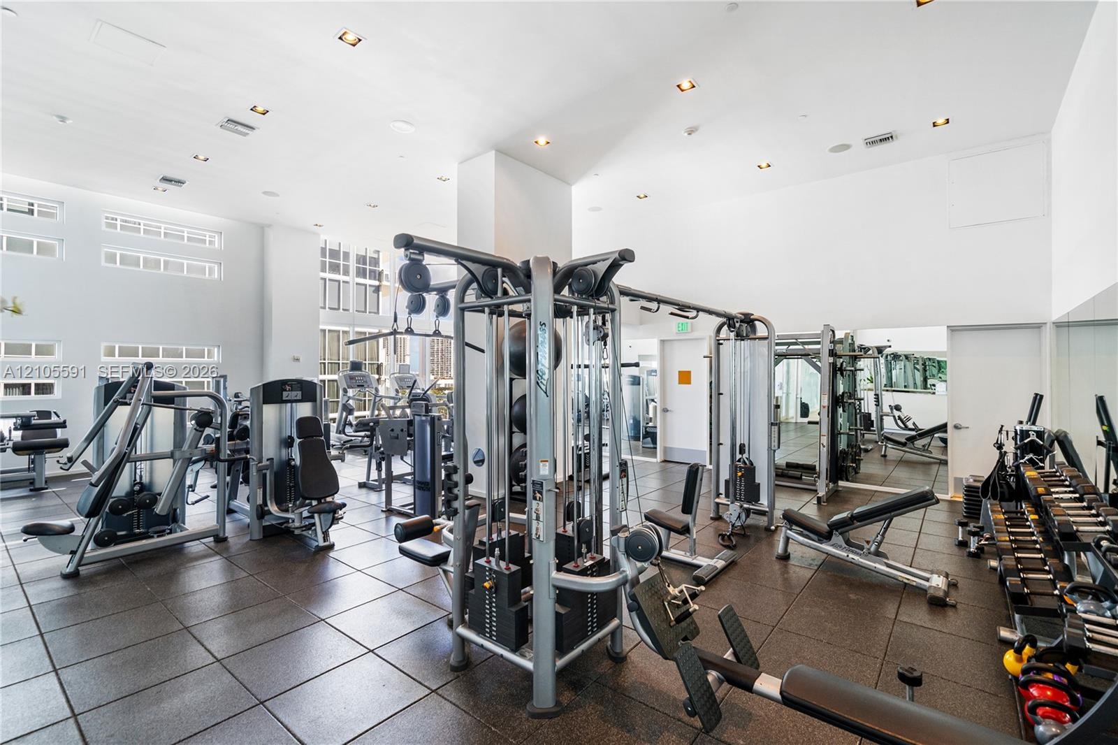 Spacious fitness area featuring rubber tile flooring, recessed lighting, and large windows
