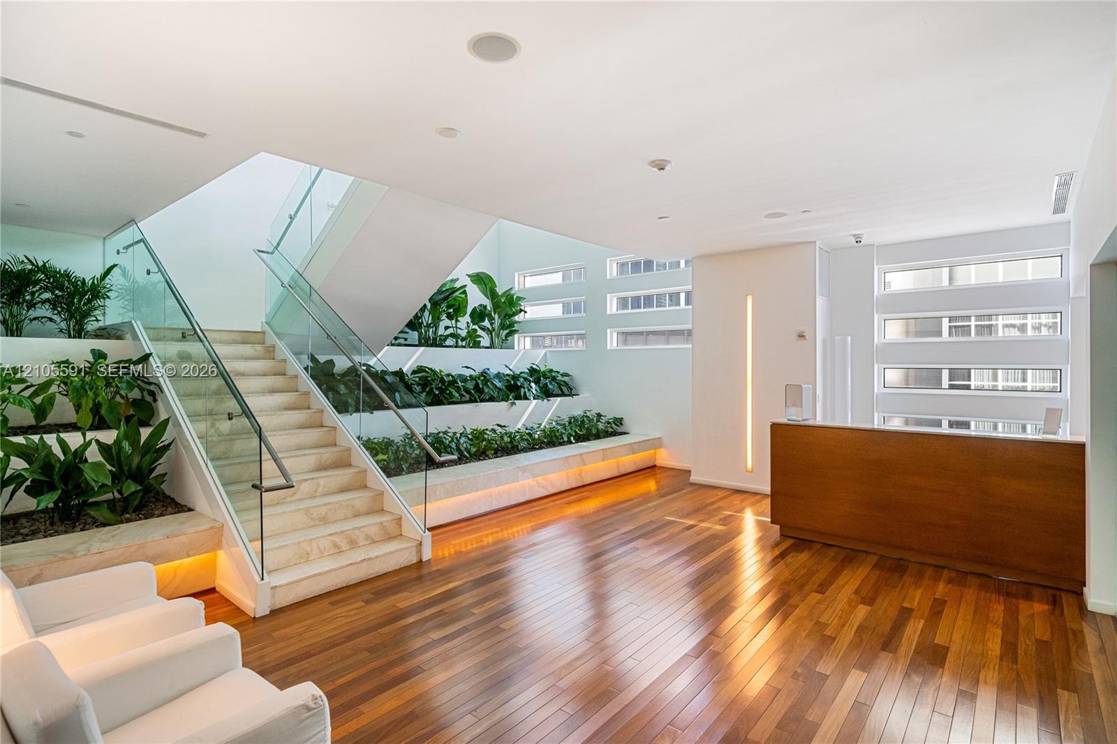Wood-finish flooring, staircase with glass railing, integrated planters, built-in reception desk, and horizontal window banks