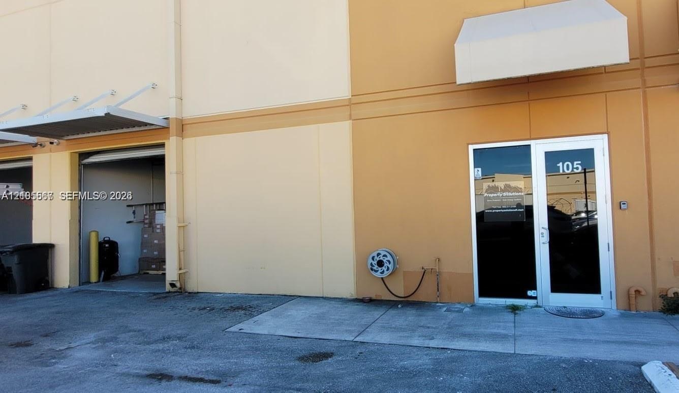 Exterior featuring two bay doors with awnings, a glass entry door with transom, and a wall-mounted hose reel