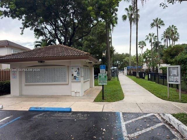 Community mailbox structure with a tiled roof, surrounded by mature palm trees and lush landscaping