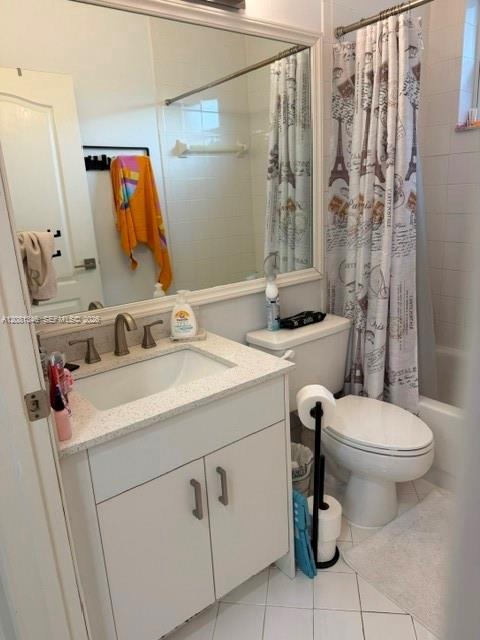 White tiled flooring, vanity with light-colored countertop, undermount sink with brushed nickel faucet, wall-mounted mirror with white frame, and a bu