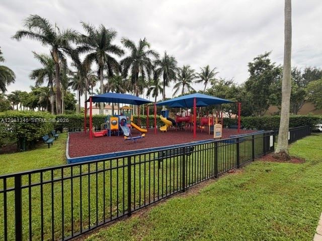 Fenced playground featuring multiple play structures, a slide, and a seesaw