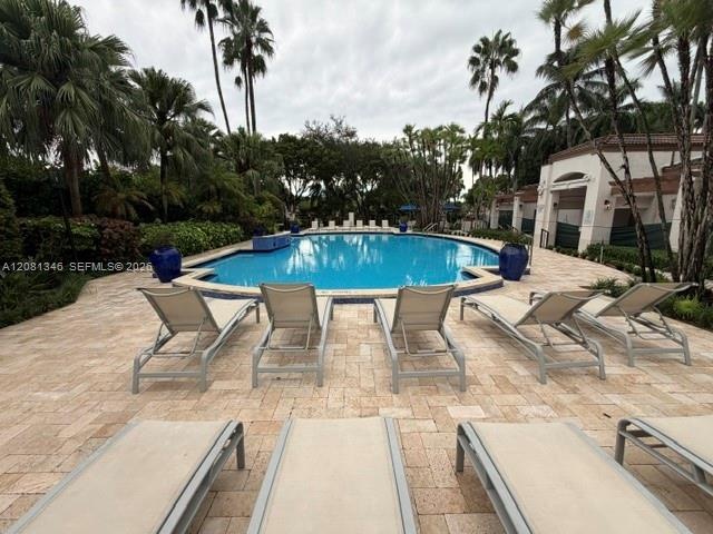 Resort-style pool area featuring a freeform pool, paver deck, lush tropical landscaping, and adjacent cabana structures