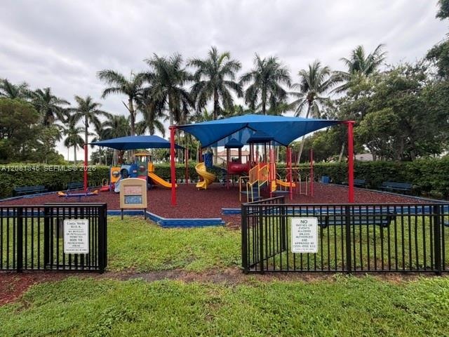 Playground area featuring multiple slides, climbing structures, and a seesaw, all shaded by blue canopies