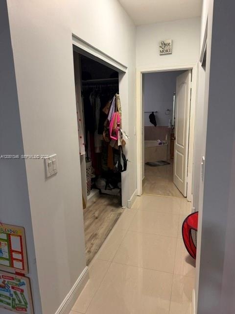 Hallway with light tile flooring, leading to an open doorway with a full bathroom beyond