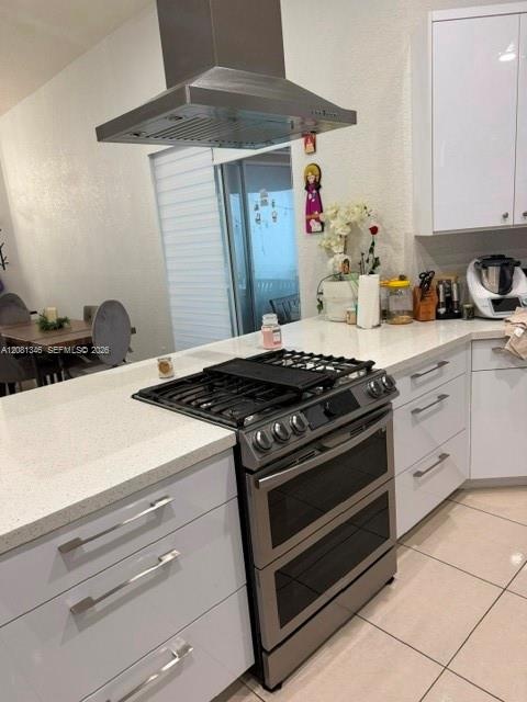 Stainless steel range hood, built-in gas range, white flat-panel cabinetry, light-toned countertop, and tiled flooring