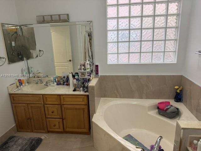 Built-in soaking tub with a tiled surround, glass block window, and an extended vanity with an integrated sink and base cabinetry