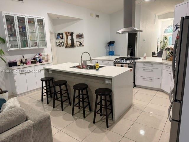 Contemporary kitchen featuring white cabinetry, a central island with an integrated sink, stainless steel appliances, and tile flooring