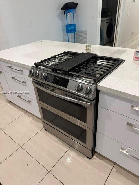 Stainless steel range with double oven, gas cooktop, white cabinetry, integrated drawer pulls, and light-toned countertops