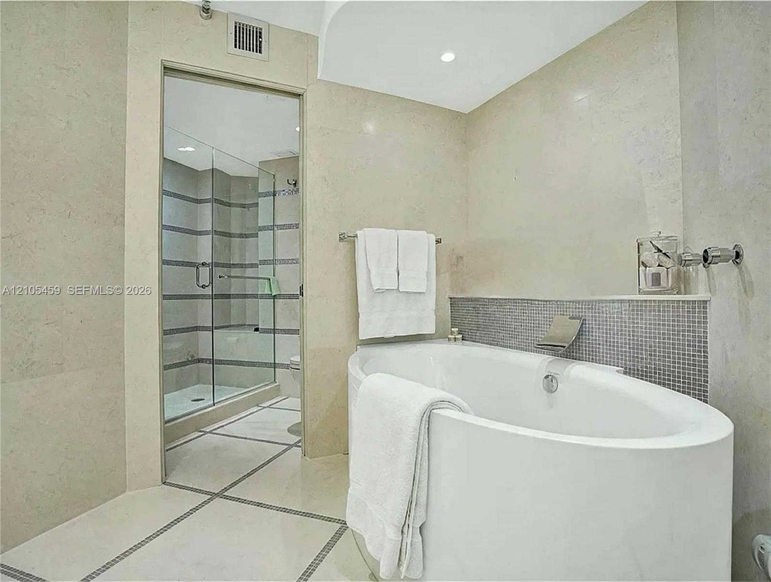 Freestanding soaking tub with a tiled surround, glass-enclosed shower, and recessed lighting
