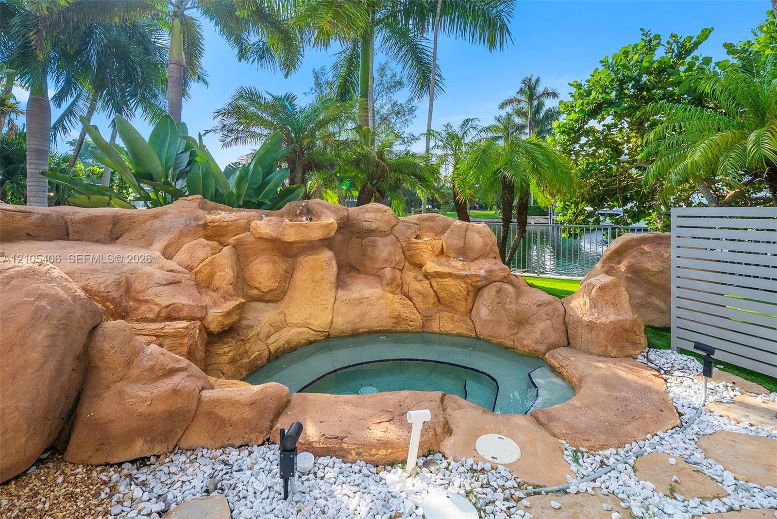 Rock-sculpted spa with integrated water feature, surrounded by white gravel and stone paving