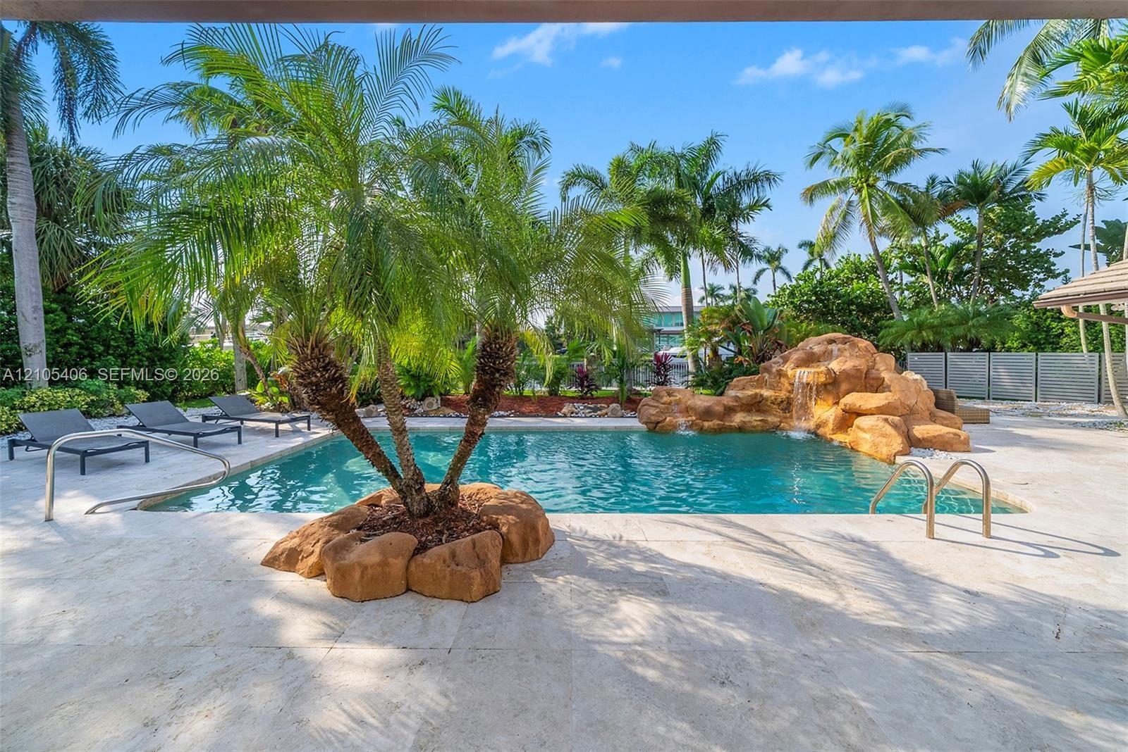 Outdoor swimming pool with a rock waterfall feature, integrated palm tree planting, and surrounding hardscaping