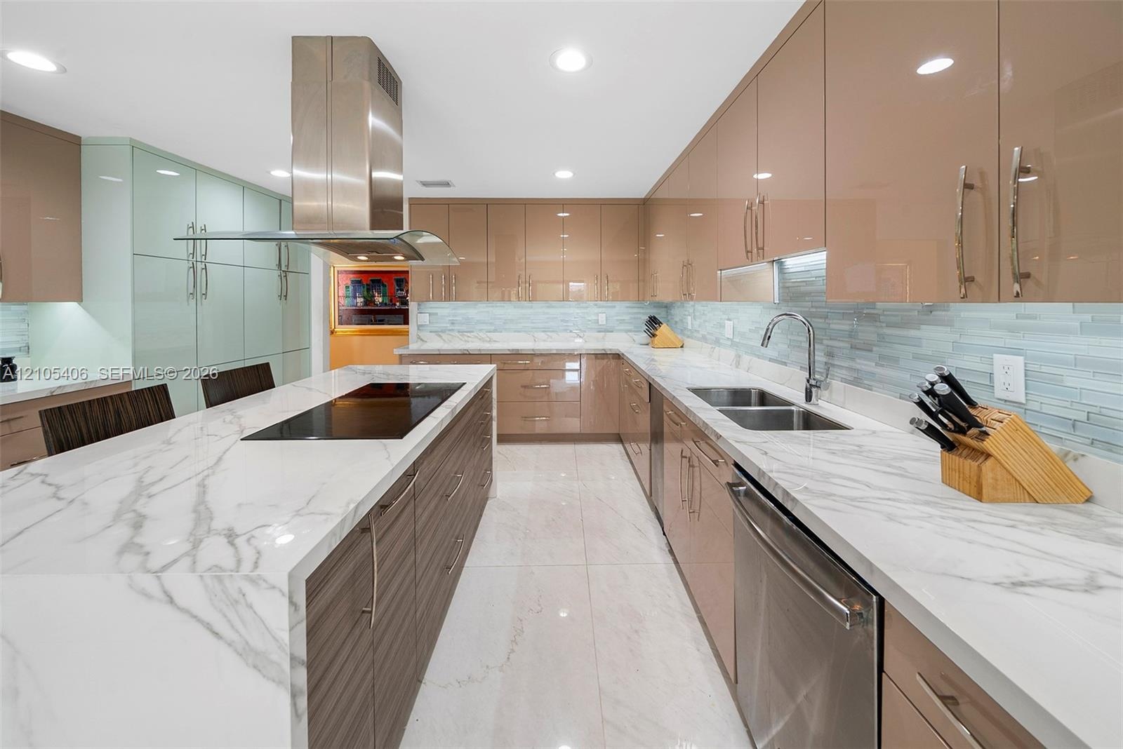Kitchen featuring a large island with an integrated cooktop, white marble-style countertops, glossy tan cabinetry, a stainless steel range hood, and a