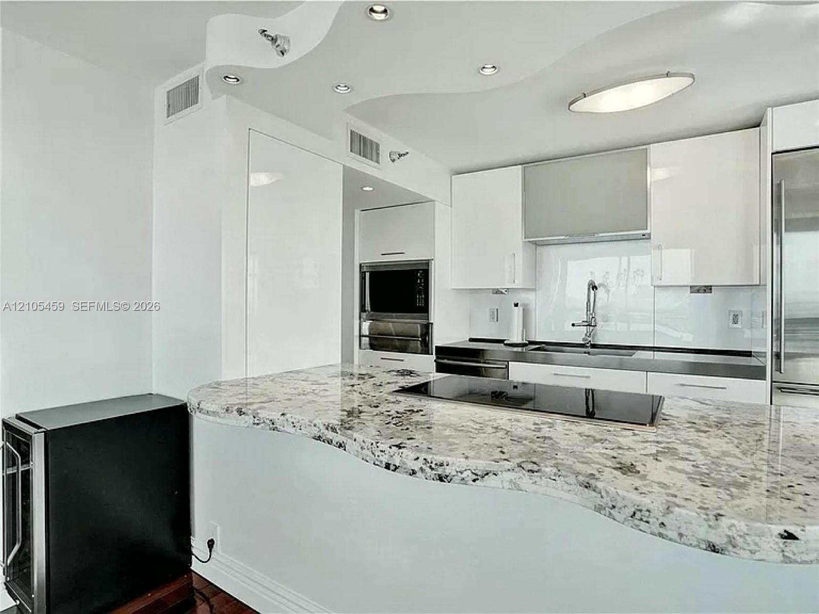 Kitchen featuring a curved stone countertop, built-in cooktop, white upper cabinetry, and a stainless steel oven