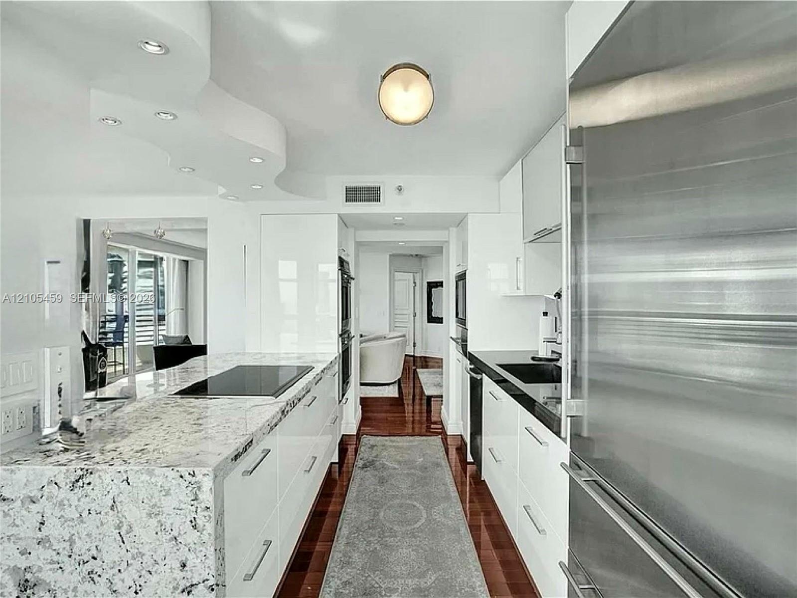 Modern kitchen featuring high-gloss white cabinetry, integrated stainless steel appliances, and wood-finish flooring