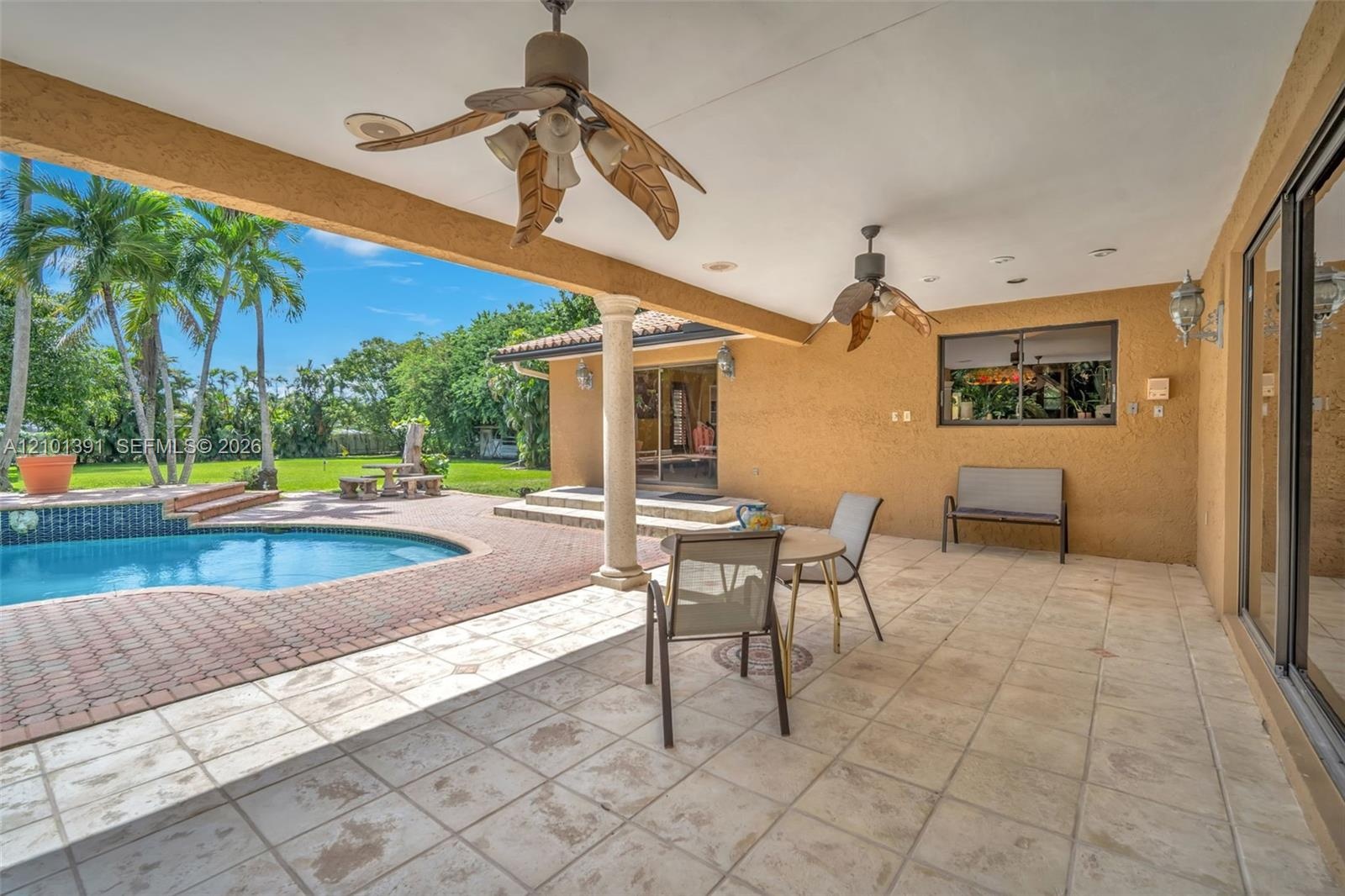 Covered patio with integrated ceiling fans, a freeform swimming pool with brick paver surround, and a manicured lawn