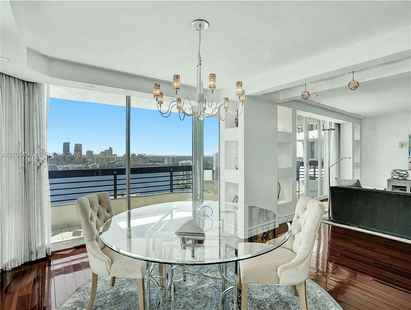 Expansive floor-to-ceiling windows, dark wood-finish flooring, recessed lighting, built-in shelving, and a modern chandelier