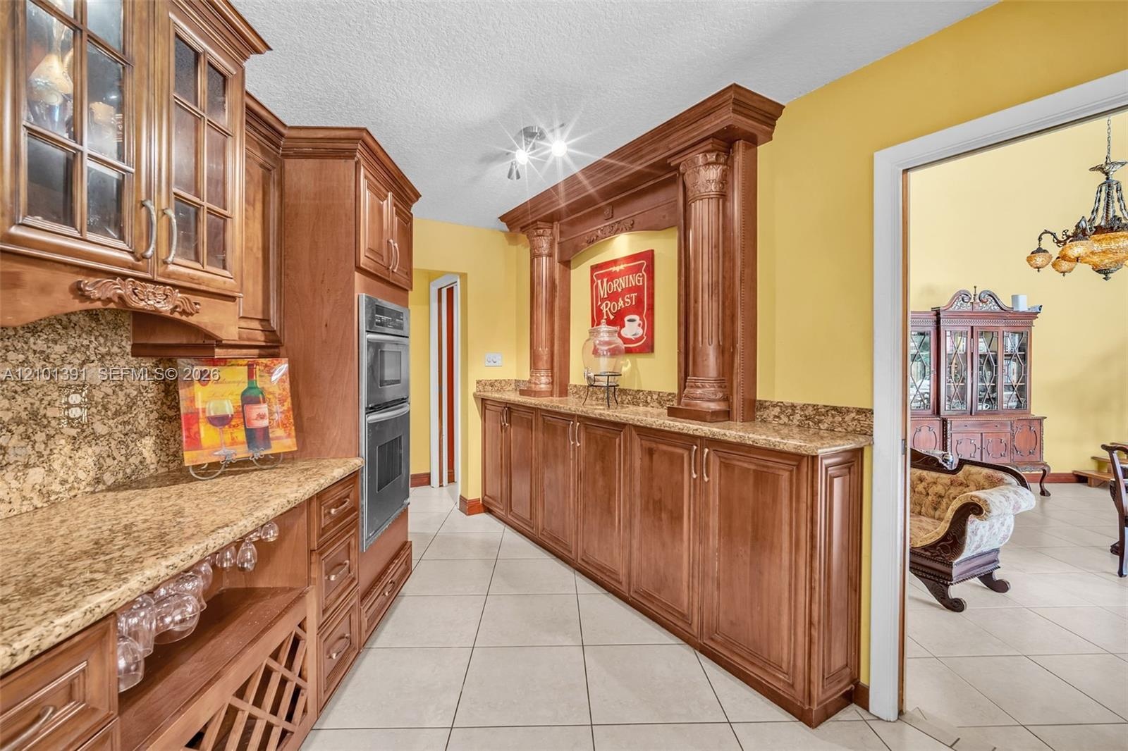 Kitchen featuring extensive wood cabinetry, granite countertops, built-in double ovens, a wine rack, and tile flooring