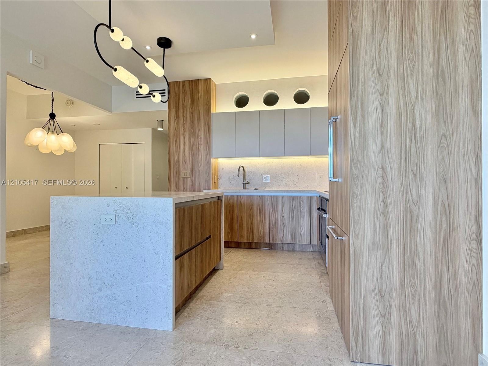 Kitchen featuring wood-finish cabinetry, a large center island with a light-toned countertop, integrated refrigeration, and unique overhead lighting f