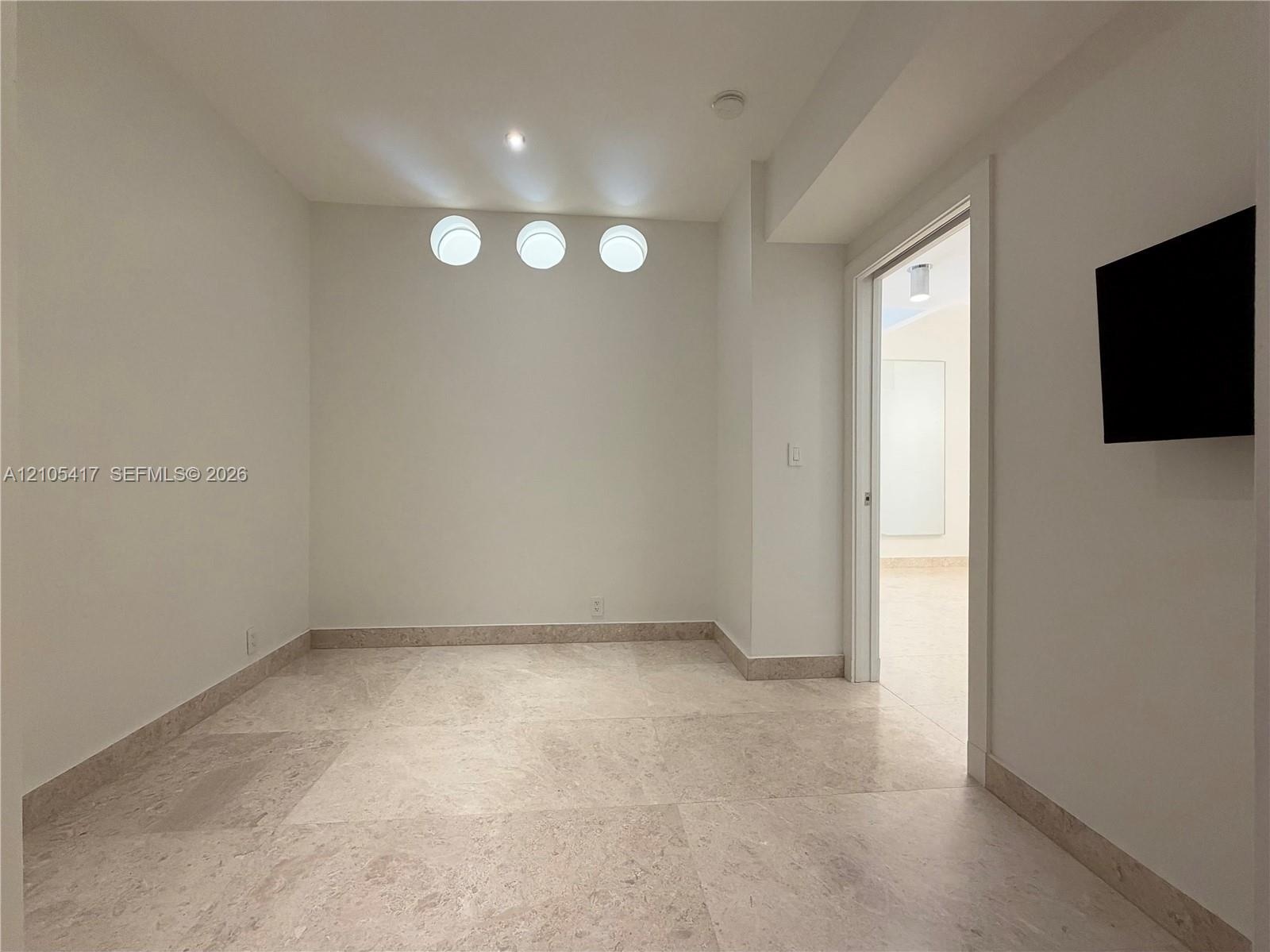 Recessed ceiling lighting, three flush-mount wall sconces, neutral wall paint, and stone tile flooring