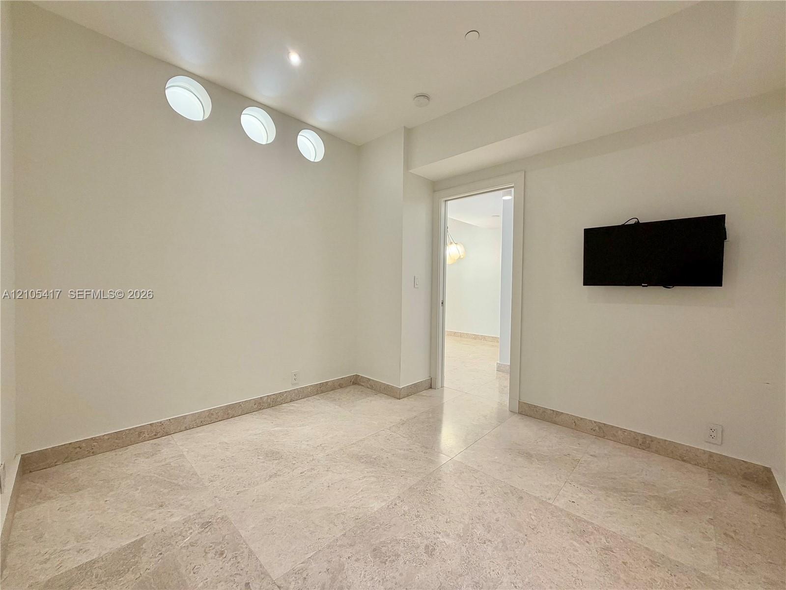 Recessed lighting, three circular wall cutouts, light-toned stone tile flooring, and a cased doorway