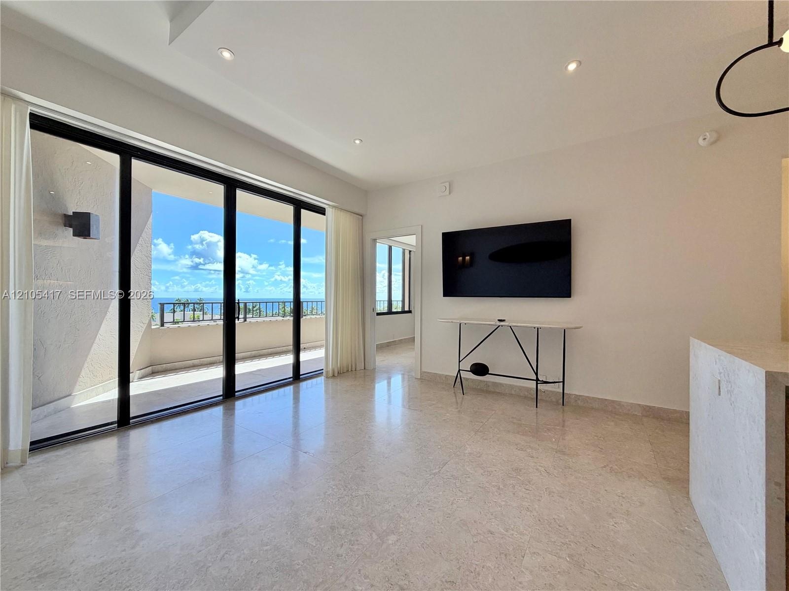 Large-format tile flooring, recessed ceiling lighting, a wall-mounted flat-screen television, a built-in wall niche, and sliding glass balcony doors