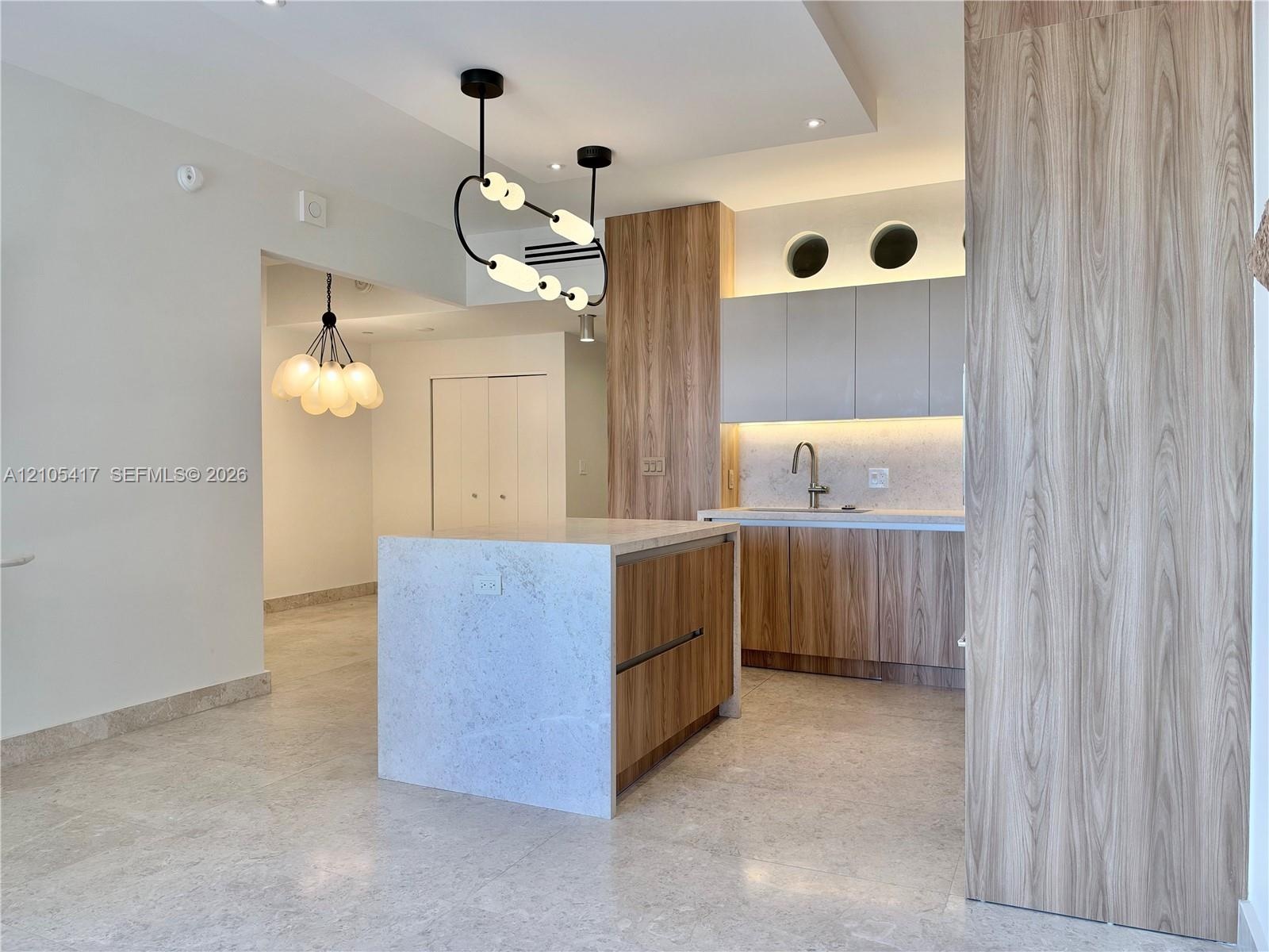 Kitchen featuring a central island with a stone countertop, wood-finish cabinetry, under-cabinet lighting, and a stainless steel sink with a gooseneck