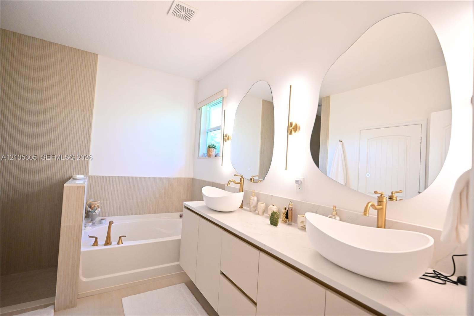 Dual vessel sinks, expansive vanity, built-in bathtub, irregular-shaped mirrors, and gold-tone fixtures