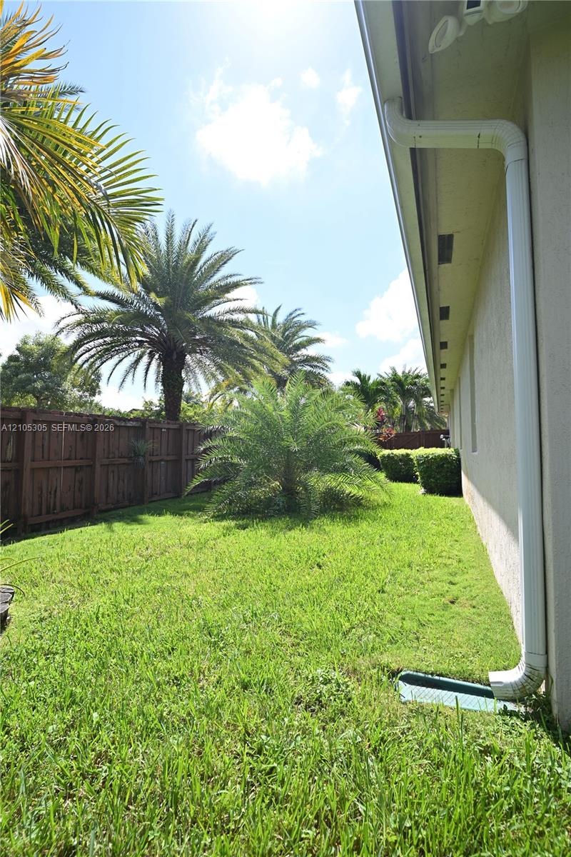 Expansive side yard featuring a manicured lawn, established palm trees, and a wood privacy fence