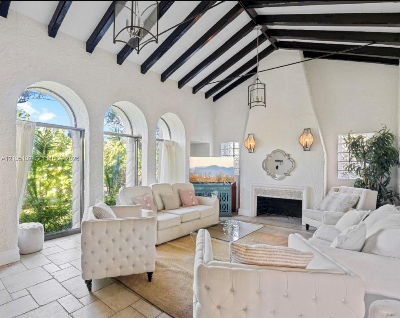 Vaulted ceilings with exposed beams, arched windows, stone tile flooring, and a built-in fireplace