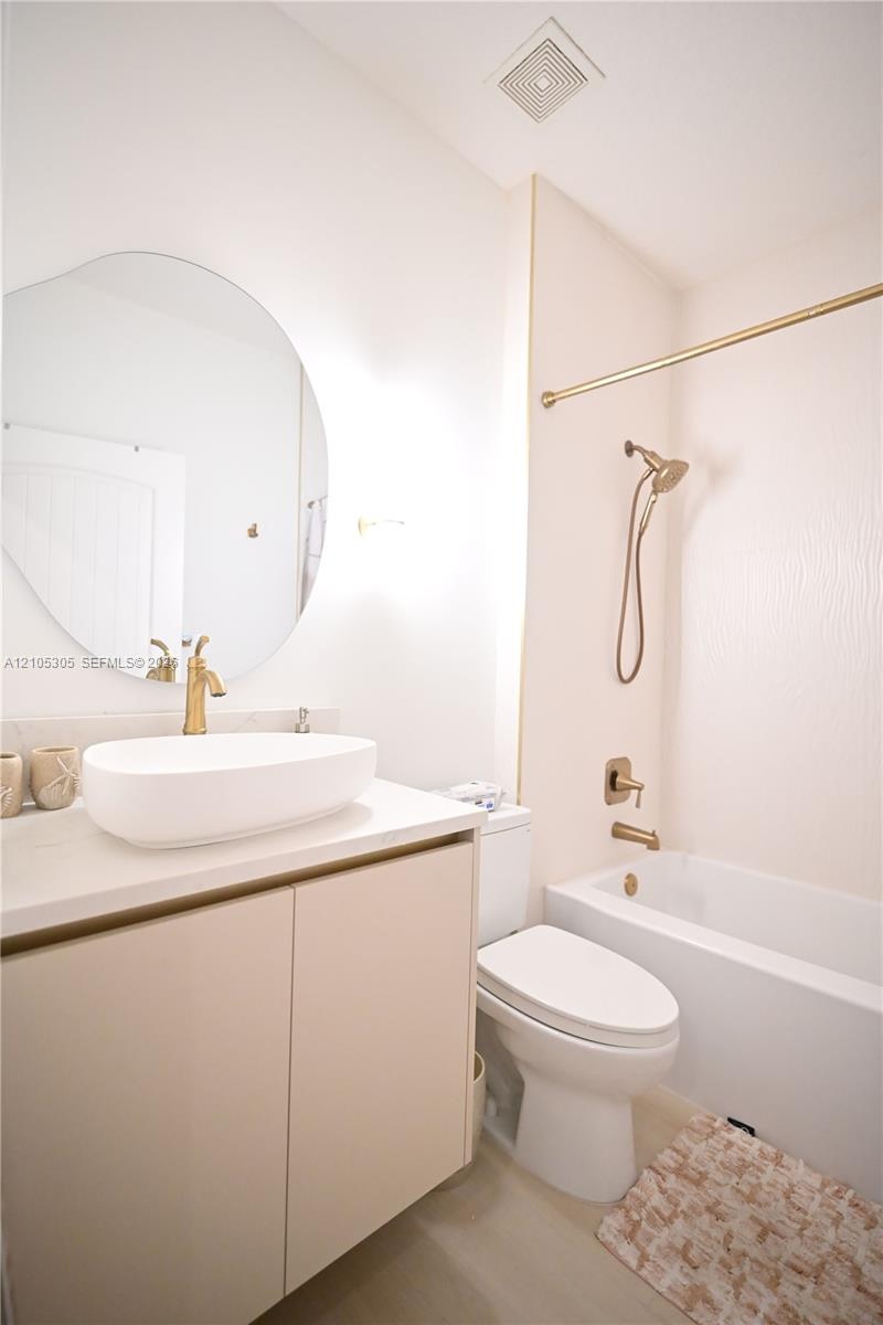 White rectangular soaking tub with a bronze-finish faucet, an oval vessel sink, and a two-door vanity
