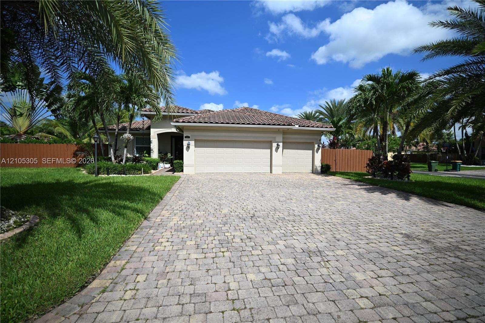 Paved driveway leading to a two-car garage, mature palm trees, and a terracotta tile roof