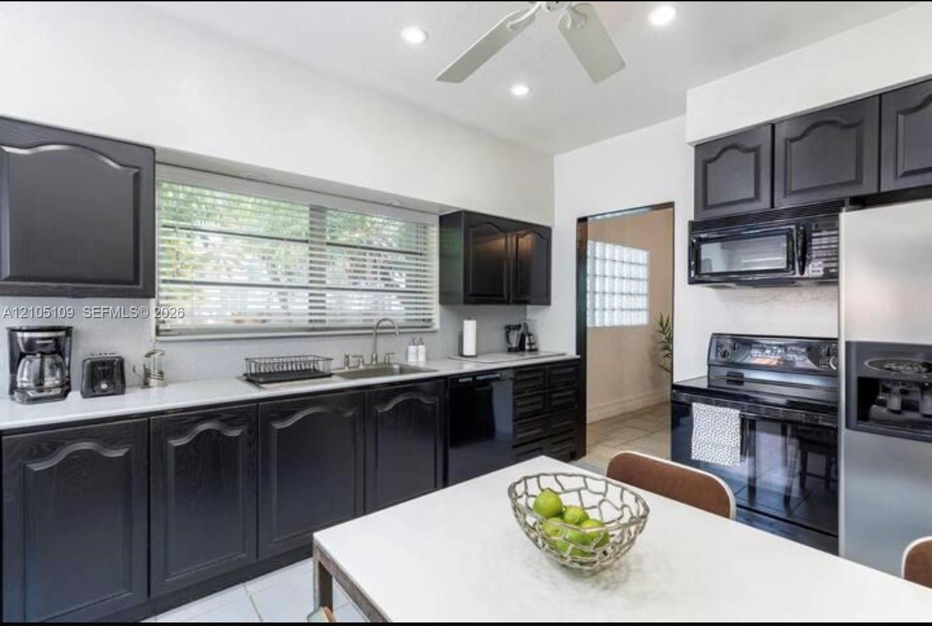 Kitchen featuring black cabinetry, white countertops, stainless steel sink, a stainless steel refrigerator, and a built-in microwave