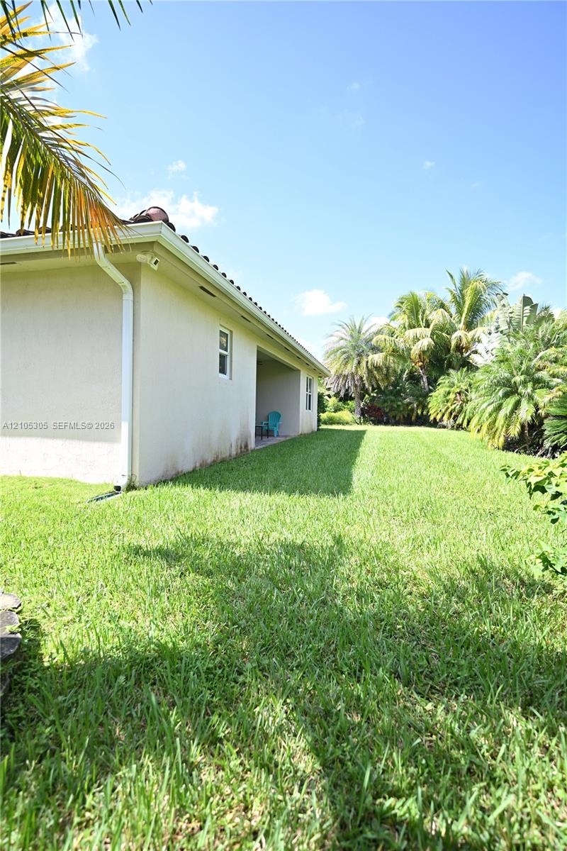 Expansive side yard featuring a lush lawn, stucco exterior, and red tile roof