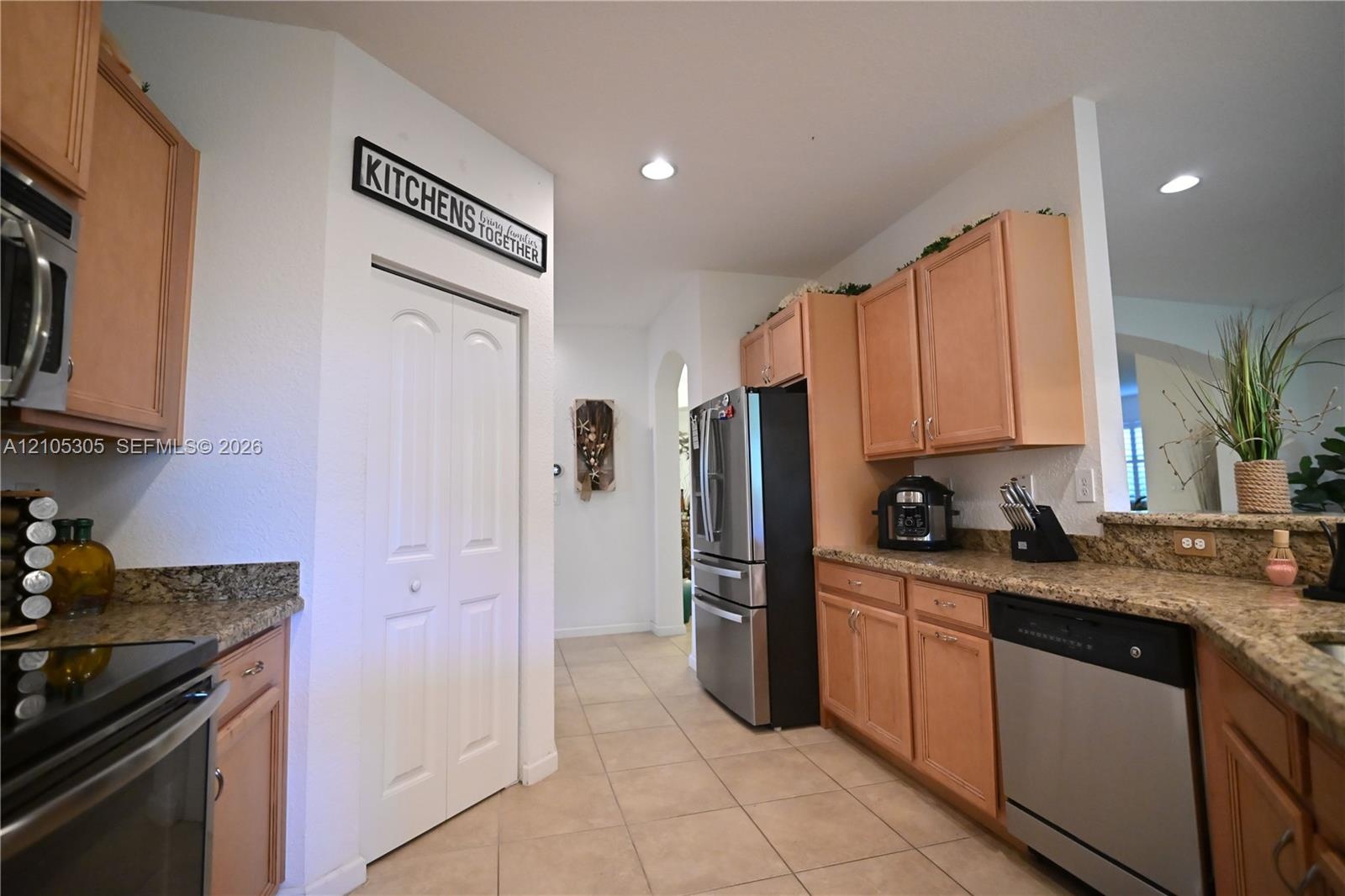 Kitchen with light wood-finish cabinetry, granite-style countertops, stainless steel appliances, and tile flooring