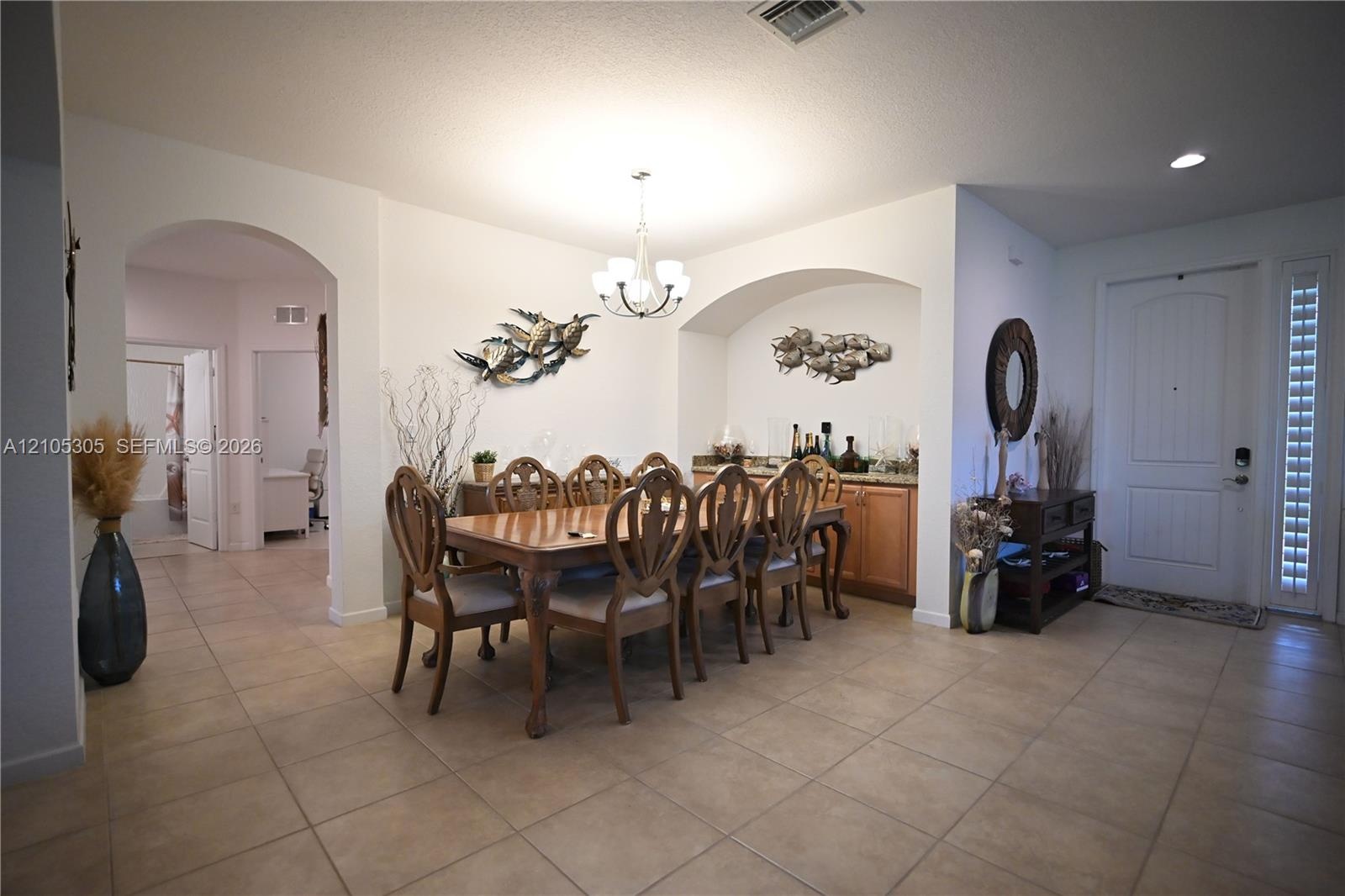 Tiled flooring throughout, featuring an arched entryway, a built-in wet bar, and a paneled front door with a textured glass sidelight