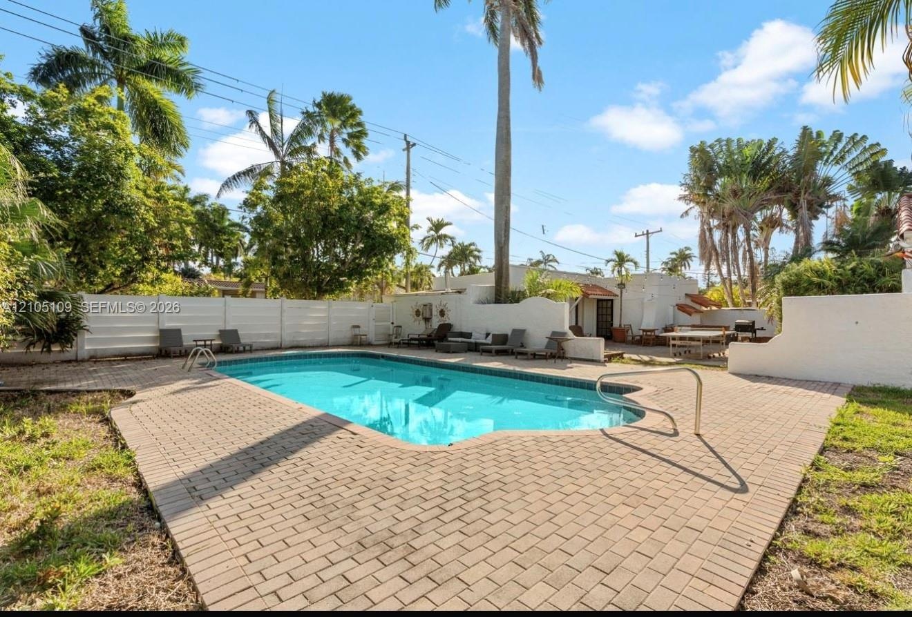 Swimming pool with brick paver surround, privacy fencing, and tropical landscaping