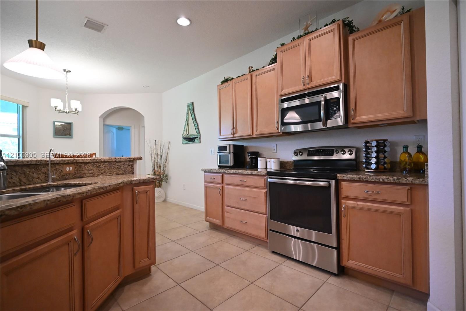 Kitchen featuring a stainless steel range, built-in microwave, wood cabinetry, stone countertops, and tile flooring