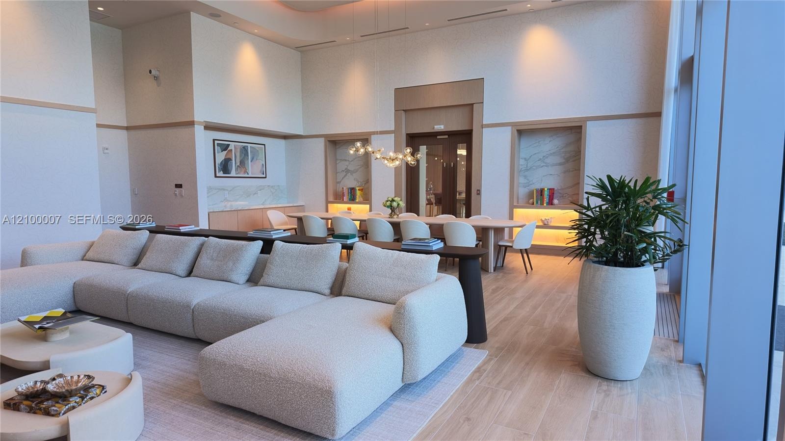 Open-concept common area featuring high ceilings, light wood-finish flooring, and built-in shelving with integrated lighting
