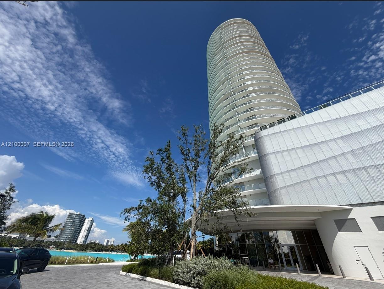 Modern high-rise building with extensive glass balconies, a curved facade, and a covered entry