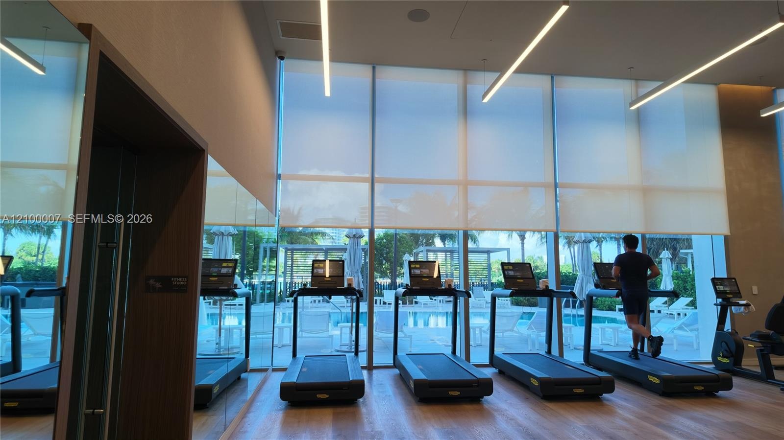 Floor-to-ceiling windows with roller shades, wood-finish flooring, recessed linear lighting, and integrated mirrors