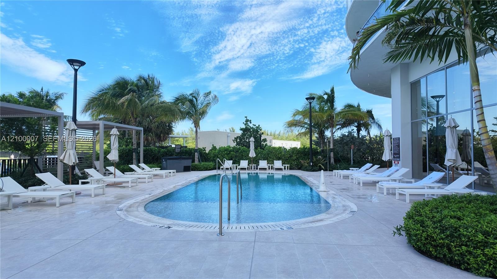 Outdoor swimming pool with integrated steps, surrounded by a paved deck, multiple lounge chairs, and pergolas