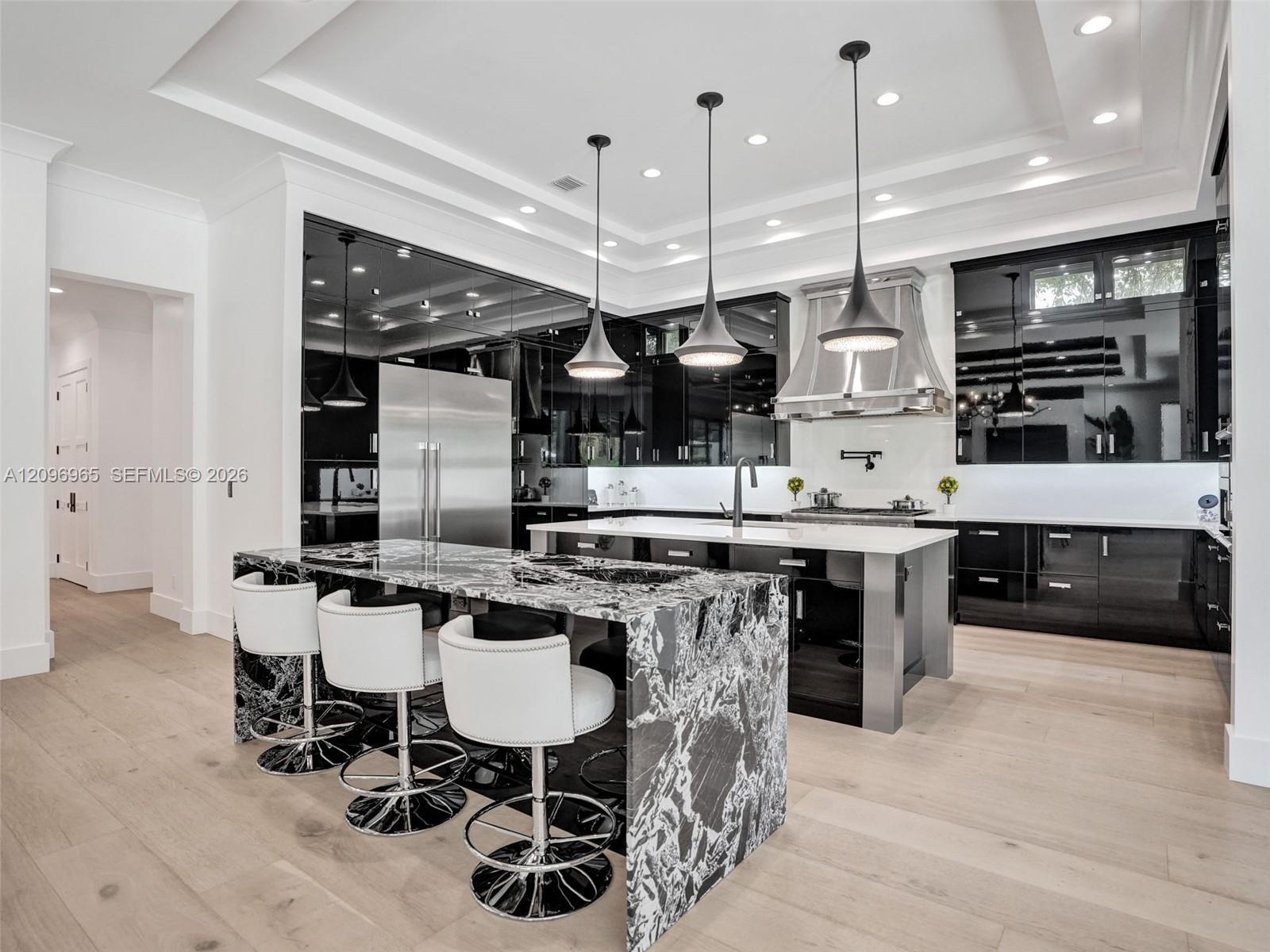 Open-concept kitchen featuring high-gloss cabinetry, a waterfall-edge stone island, wood-finish flooring, a coffered ceiling with a black wood-plank i