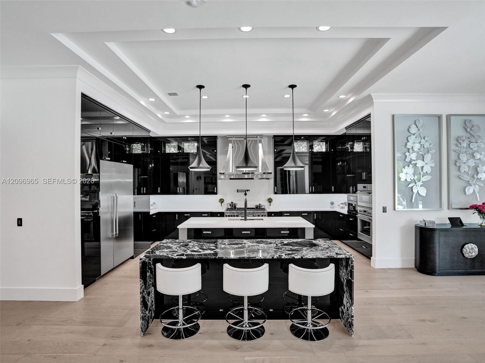 Open-concept living space featuring wood-finish flooring, a coffered ceiling with dark-toned plank inlay, recessed lighting, and a tiered metal chande